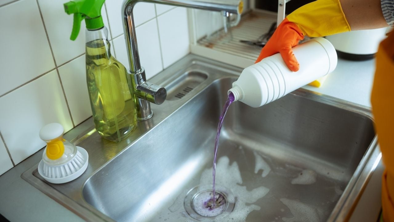homeowner using drain cleaner to unclog kitchen sink drain.
